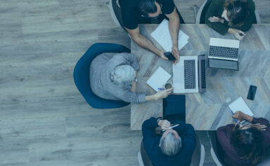 Overhead photo of five people sitting at a table in an office