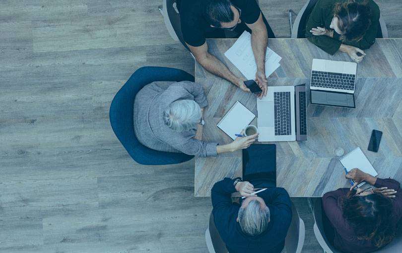 Overhead photo of five people sitting at a table in an office