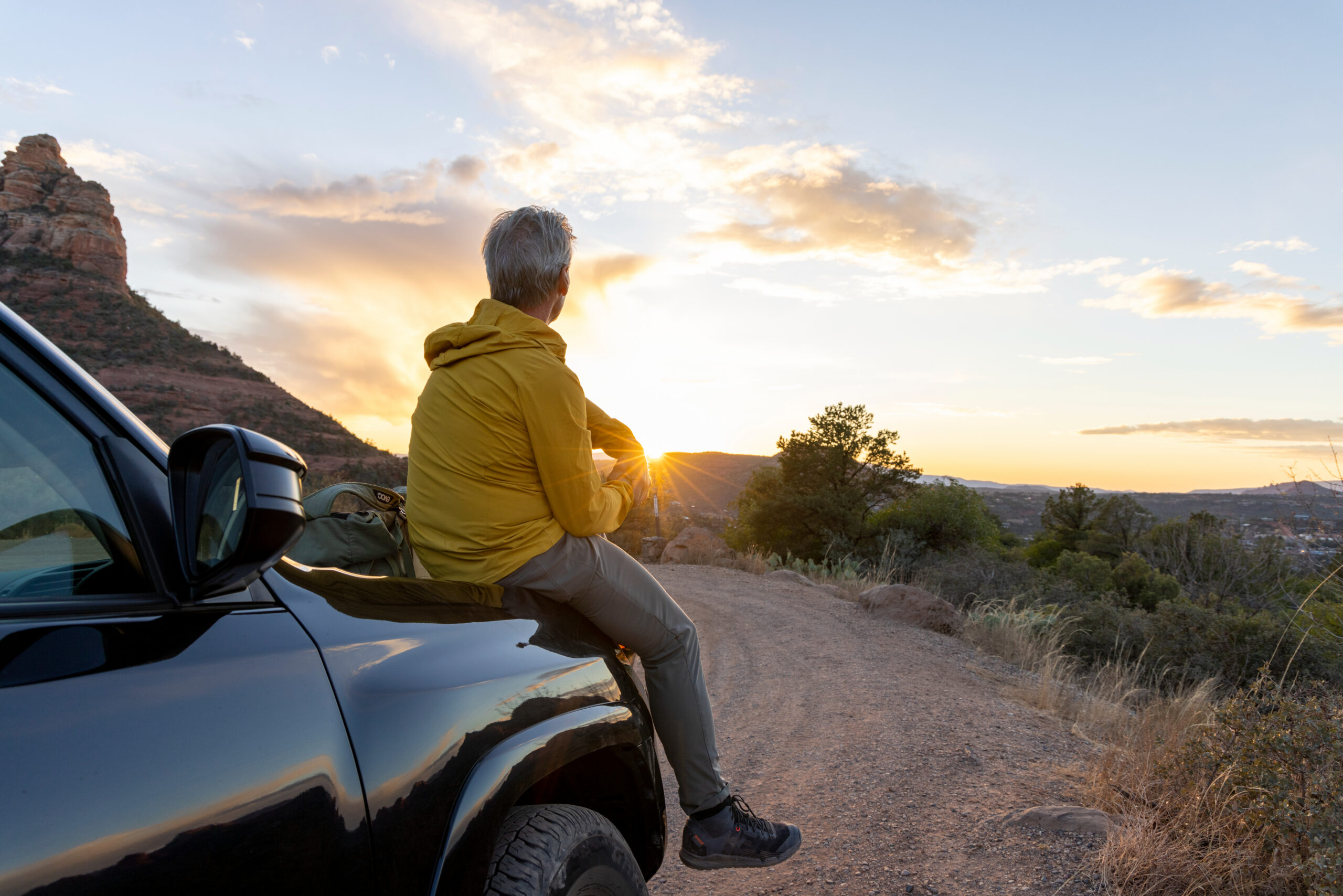 Man Sitting on Car at Sunset in the Mountains